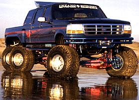 1983 Ford Bronco - Custom 6-wheel pickup truck with large tires and lifted suspension on wet sand.