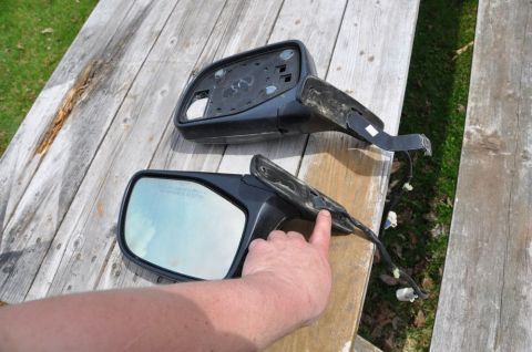 1996 Ford Bronco - Two black side mirrors with wiring harnesses are displayed on a wooden surface, with a hand pointing to one of them.