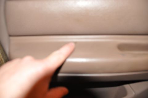 1996 Ford Bronco - A finger points to a small imperfection on the interior door panel of a vehicle.