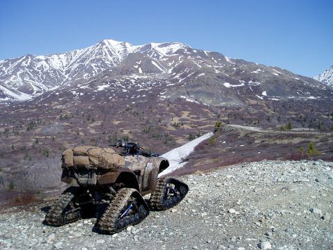 2000 Ford E350 - A camouflage-patterned ATV with tracks instead of wheels is parked on a rocky, gravelly slope with snow patches visible in the background.…