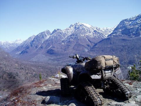 2000 Ford E350 - A camouflage-patterned ATV with tracks instead of wheels is parked on a rocky overlook, facing away from the camera. The ATV is loaded with…