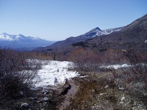 2000 Ford E350 - A scenic mountain landscape with snow patches and a muddy trail in the foreground under a clear blue sky.