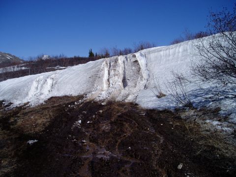 2000 Ford E350 - A snow-covered hillside with melting snow creating streaks down the muddy slope under a clear blue sky.