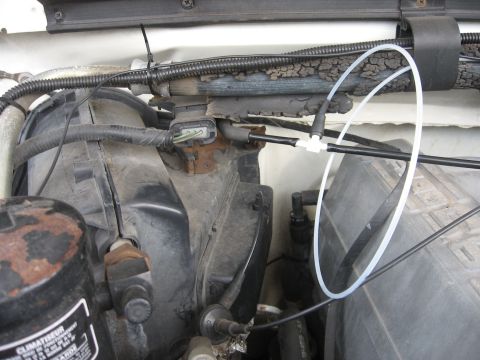 1990 Ford F-150 - A close-up view of the engine bay of a 1990 Ford F-150, showing various hoses, wiring, and engine components. A white plastic tube is loope…