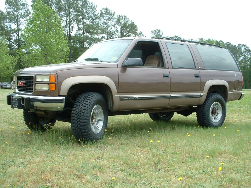 Brown two-tone GMC Suburban 2500 SUV lifted on off-road tires in a grassy field