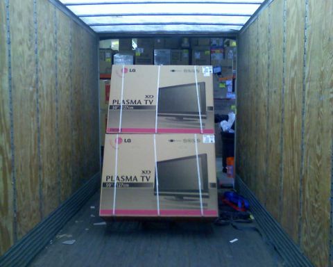 2006 Ford E350 - Two stacked boxes of LG Plasma TVs are loaded into the back of a cargo trailer. The trailer has wooden walls and a corrugated metal floor.