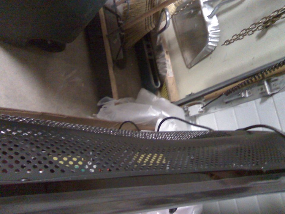 Perforated metal surface with colorful items behind it, dustpan and broom in background.