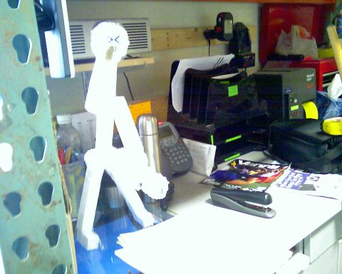 2006 Ford E350 - A white, abstract sculpture with a face drawn on its head sits on a desk next to a cordless phone, a stapler, and a paper organizer.