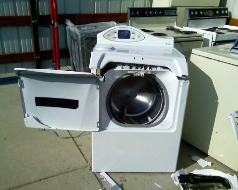 2006 Ford E350 - A white front-loading washing machine with its door open sits on a concrete surface. The washing machine is damaged, with pieces of white p…