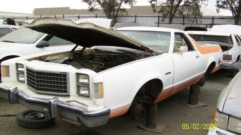 1972 Ford Ranchero - A white 1972 Ford Ranchero with an orange stripe sits on blocks in a junkyard with its hood open.