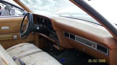 1972 Ford Ranchero - Tan interior of a worn vintage car showing the dashboard, round steering wheel and bench seat, apparently in a salvage yard.