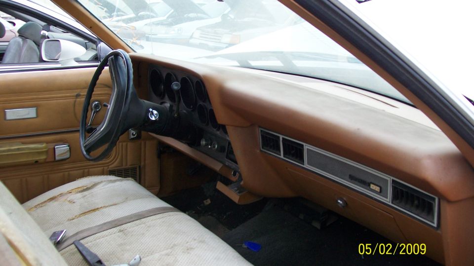 Tan vintage car interior dashboard steering wheel and bench seat in junkyard