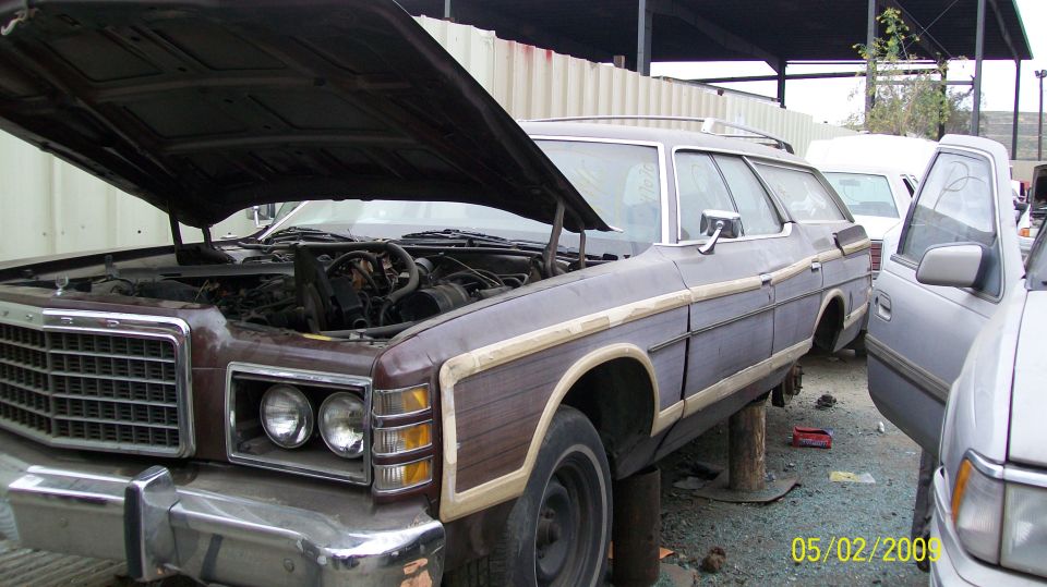 1975 Ford station wagon, wood paneling, hood open, parked in junkyard next to other vehicles