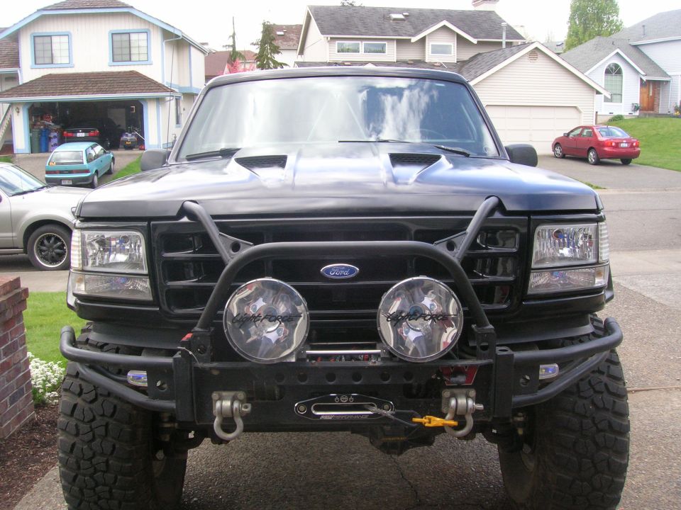 Front of black lifted Ford with tube bumper, winch, and dual round driving lights