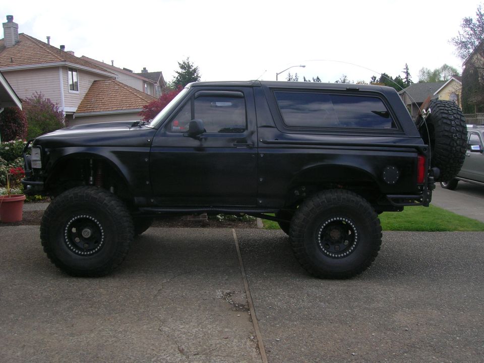 Matte black lifted two-door Ford Bronco SUV in side view on a driveway.