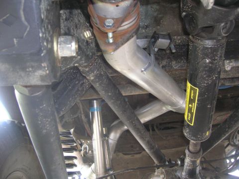 1996 Ford Bronco - Underside view of a vehicle's suspension and drivetrain components, featuring a silver exhaust system, a black shock absorber with a yellow…