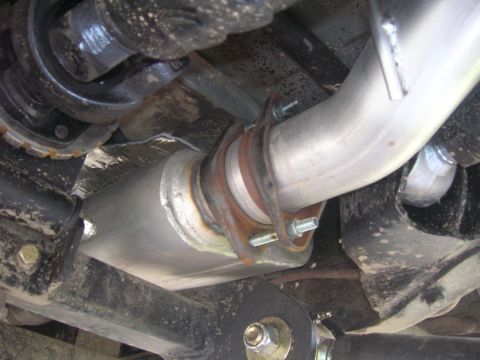 1996 Ford Bronco - The underside of a vehicle shows a section of the exhaust system, including a muffler and piping connected with a flange and bolts. The veh…