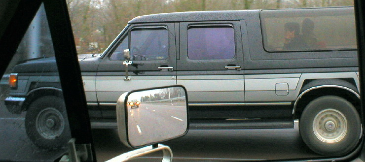 Two-tone gray and black extended van seen through car window in traffic