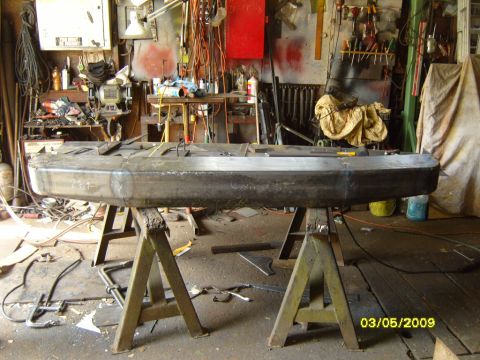 1989 Ford Bronco - A custom-fabricated rear bumper sits on sawhorses in a cluttered workshop, awaiting installation.