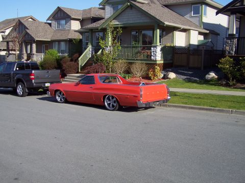 1973 Ford Ranchero - Rear three-quarter view of a lowered orange-red Ford Ranchero coupe-utility parked at the curb of a suburban street, with FORD lettering on…