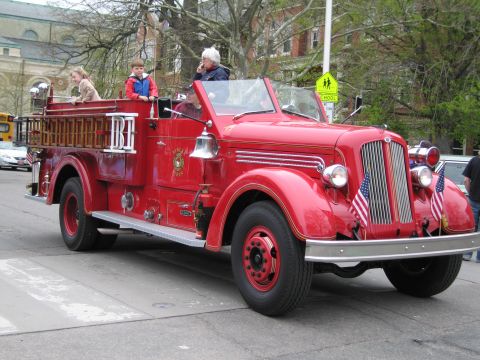 1991 Ford LTD Crown Victoria - vintage red open-cab fire engine carrying riders drives along a street in a parade, with American flags on the front.