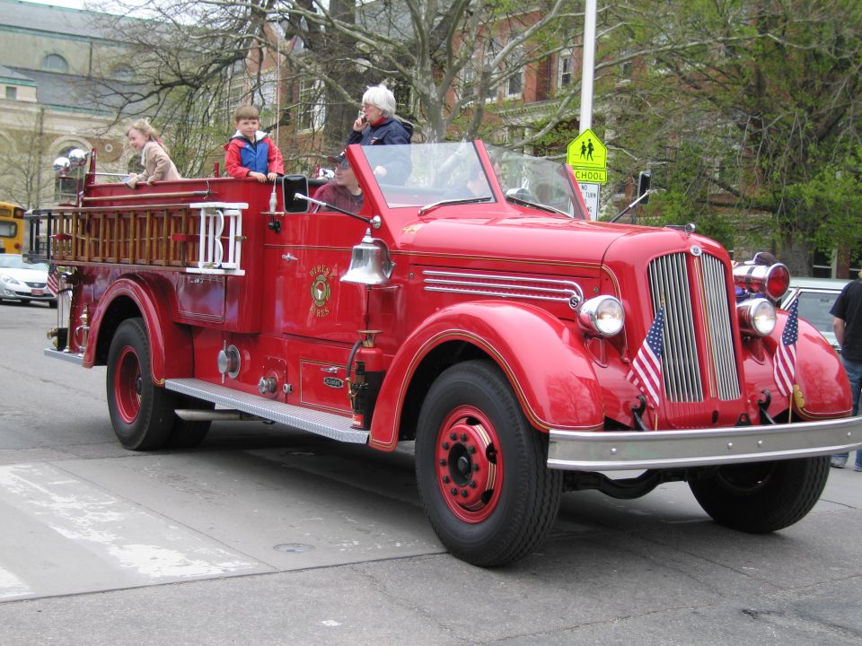 Vintage red open-cab fire engine with riders driving in a parade