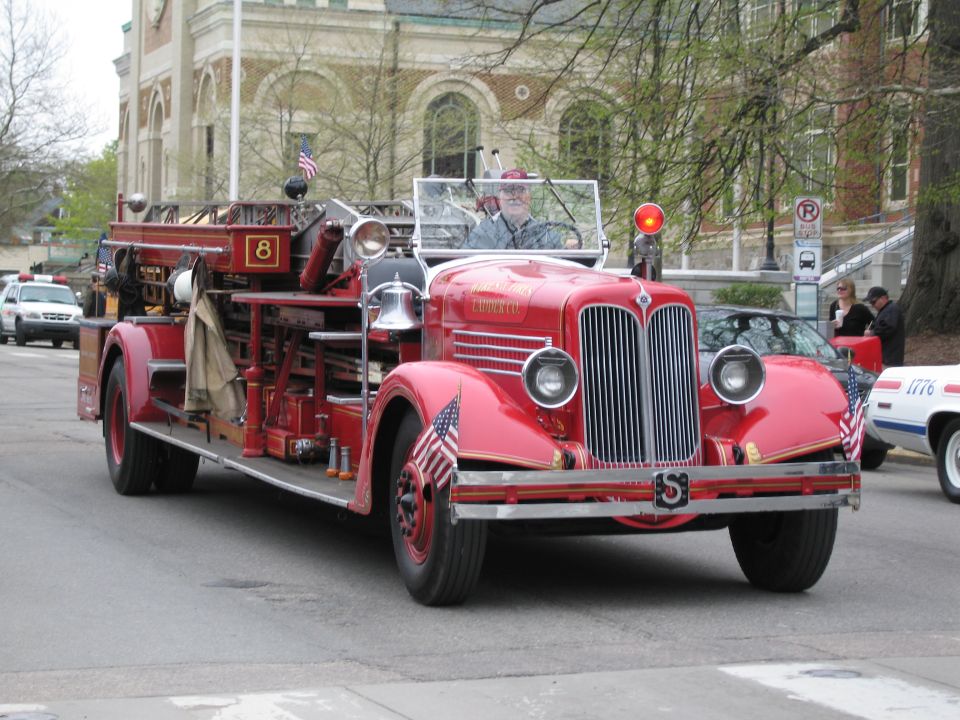 Antique red open-cab fire engine numbered 8 driving in a parade