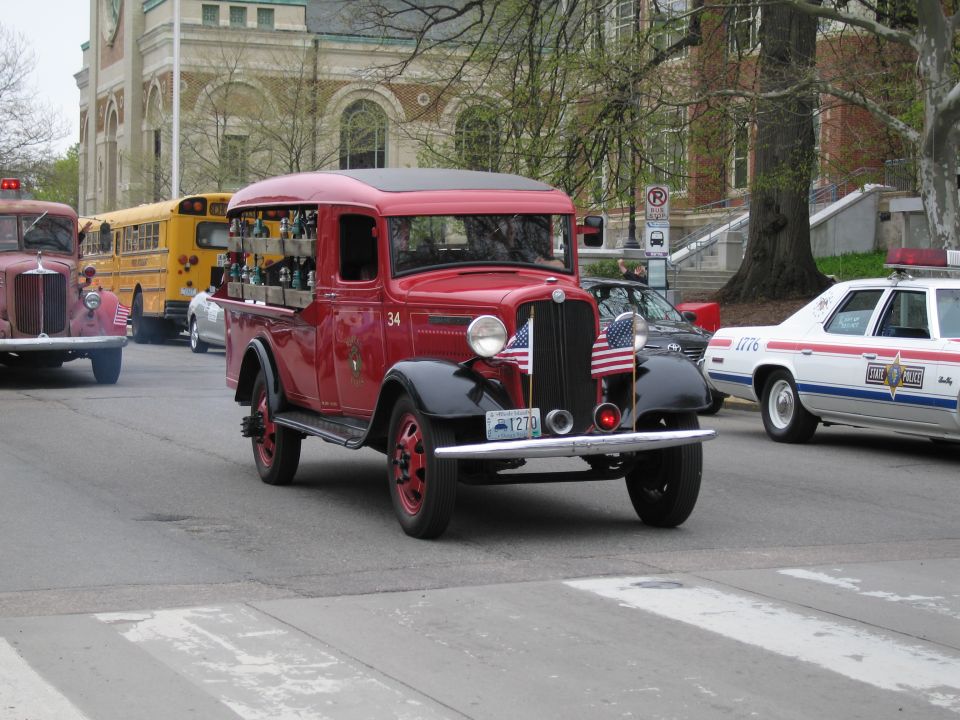 Vintage red and black fire truck numbered 34 in a parade with school bus