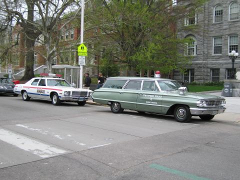 1991 Ford LTD Crown Victoria - green Stratford Police radio-patrol station wagon parks at a curb beside a white police sedan near a stone building.