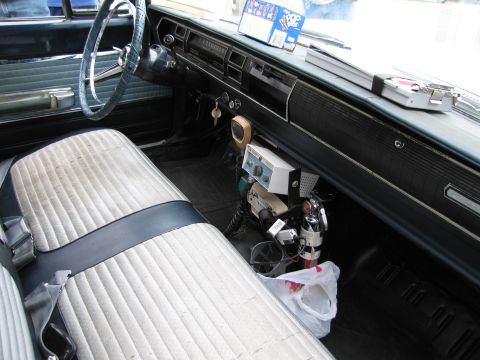 1991 Ford LTD Crown Victoria - Interior of an old sedan showing a blue steering wheel, white bench seat and a floor-mounted vintage two-way police radio.