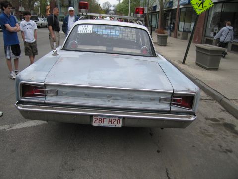 1991 Ford LTD Crown Victoria - Tail end of a silver primered classic police sedan with plate 28F H2O parked curbside as pedestrians pass on the sidewalk.