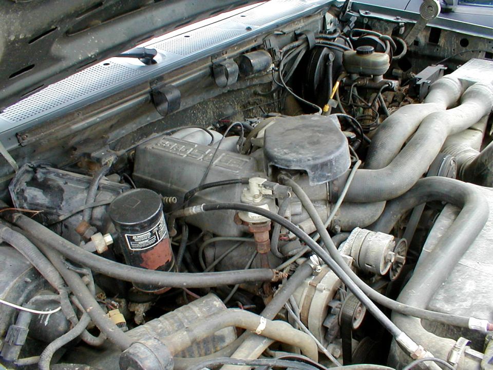 Engine bay of an older truck showing a dirty inline or V engine with hoses and air cleaner