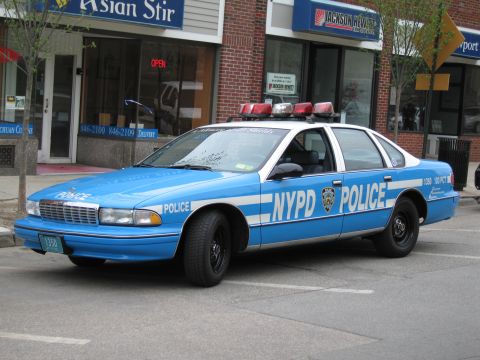 1991 Ford LTD Crown Victoria - light-blue NYPD police car with white doors and roof lightbar parked at a curb in front of an Asian Stir restaurant.