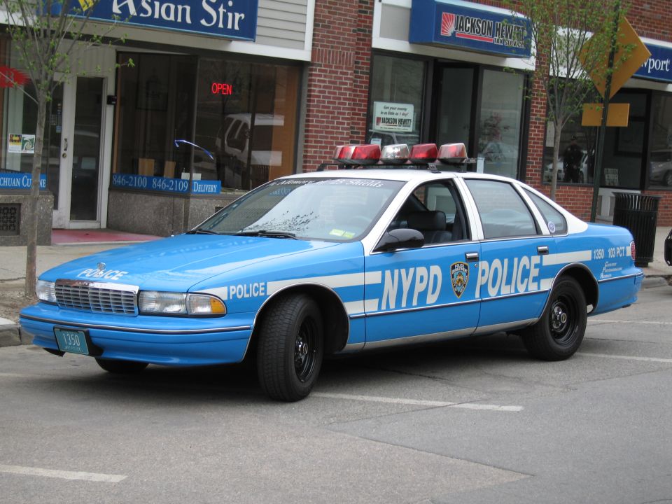 Light blue NYPD Chevrolet Caprice police car parked in front of storefronts