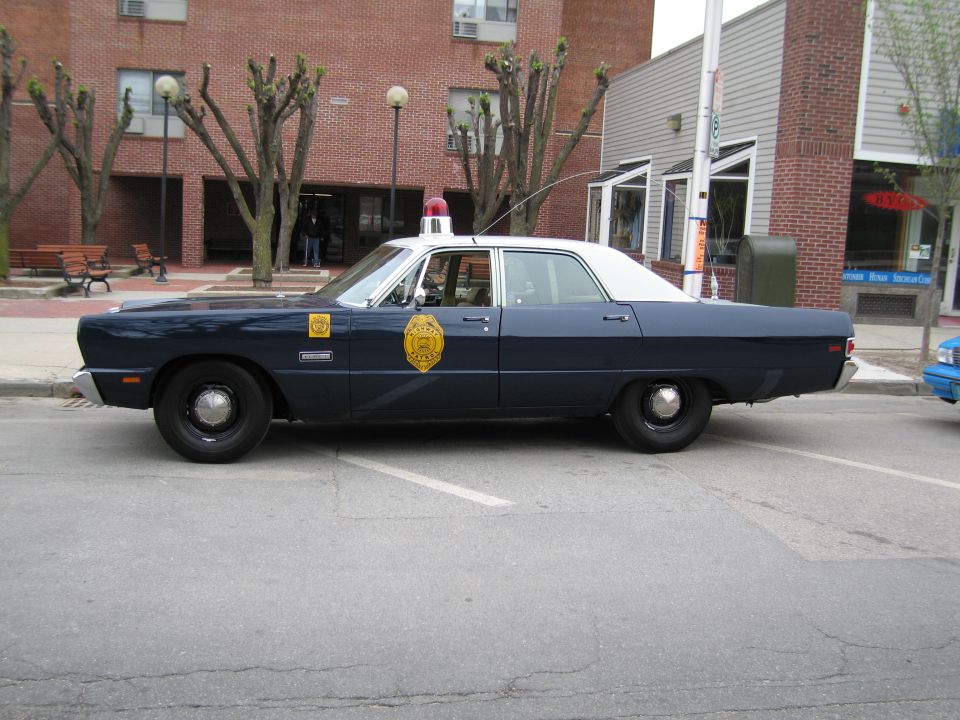 Side profile of a dark blue classic state police sedan parked along a curb