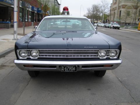 1991 Ford LTD Crown Victoria - Head-on view of a dark blue classic Plymouth police sedan with a red roof beacon, dual headlights and a New York plate reading N-67906.