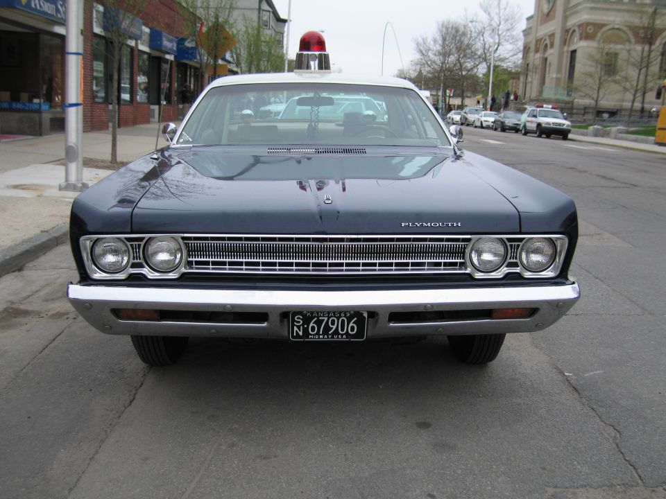 Front of a dark blue classic Plymouth police sedan with roof beacon and plate N-67906