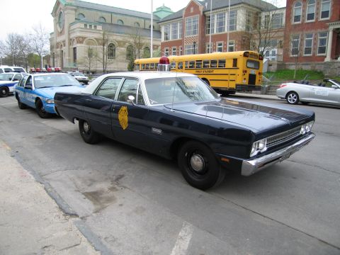 1991 Ford LTD Crown Victoria - dark blue classic Plymouth state-police sedan with gold door shield parks near a yellow school bus and an ornate stone building.