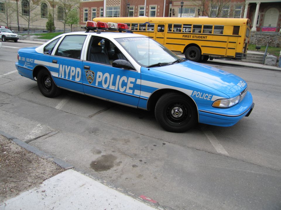 Light blue NYPD Chevrolet Caprice police car parked near a yellow school bus