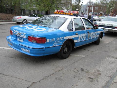 1991 Ford LTD Crown Victoria - light-blue and white NYPD police car marked '1350 103 PCT' parked on a street with other patrol cars behind it.