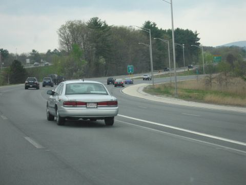1991 Ford LTD Crown Victoria - silver four-door sedan drives down a divided highway with other traffic and tree-lined median.