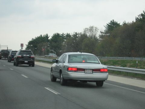 1991 Ford LTD Crown Victoria - silver Ford four-door sedan with brake lights illuminated travels on a multi-lane highway next to an SUV.