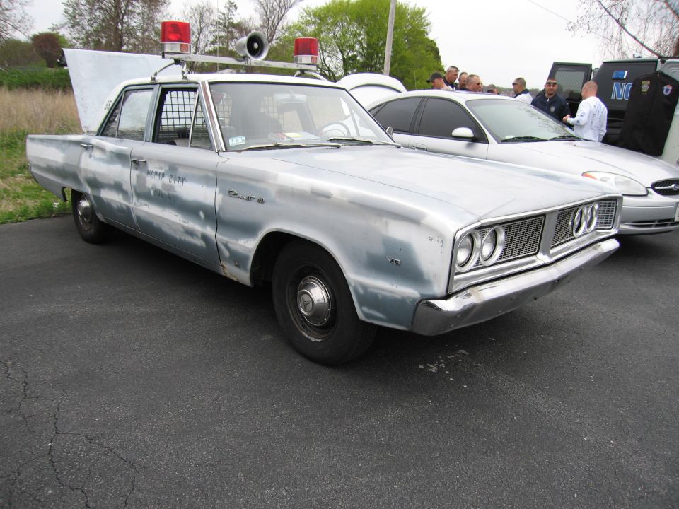 Weathered light-blue 1960s Dodge police sedan with roof lights and siren