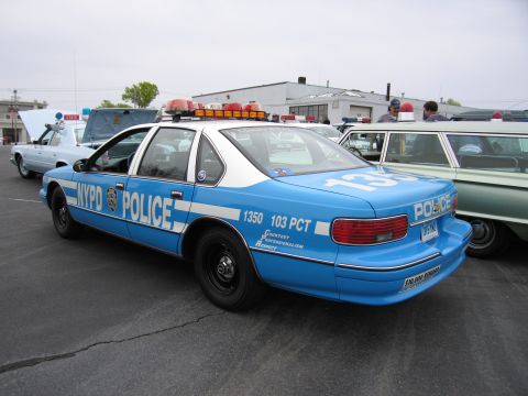 1991 Ford LTD Crown Victoria - Rear three-quarter view of a blue-and-white NYPD Chevrolet Caprice police car marked '1350 103 PCT' with an amber lightbar.
