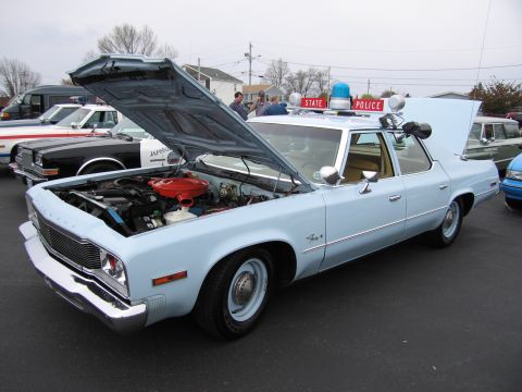 1991 Ford LTD Crown Victoria - light-blue Plymouth State Police sedan with its hood up showing the engine and a red 'STATE POLICE' roof beacon.