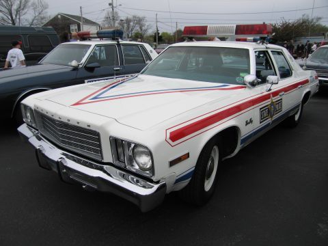 1991 Ford LTD Crown Victoria - white Plymouth State Police sedan with red and blue stripes and a roof lightbar, parked among other patrol cars.