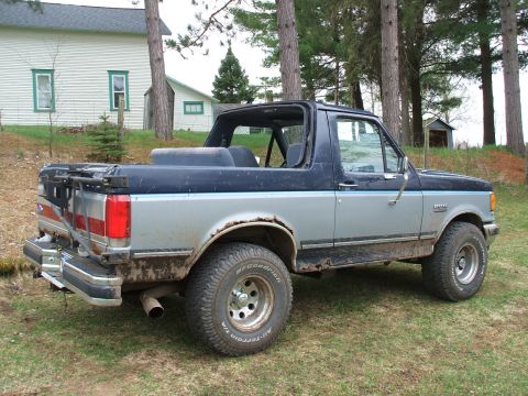 1990 Ford Bronco - A 1990 Ford Bronco is parked on a grassy area with a house and trees in the background.