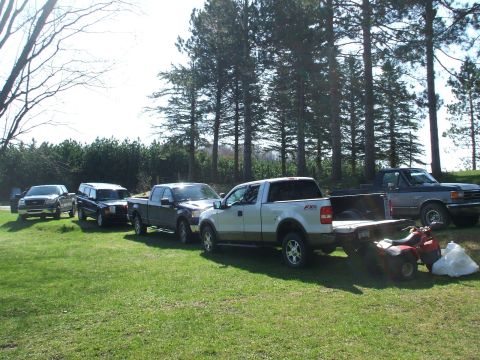 1990 Ford Bronco - A lineup of trucks and an SUV are parked on a grassy area with a line of trees behind them.
