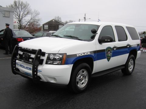 1991 Ford LTD Crown Victoria - white Chevrolet Tahoe Police SUV with a black push bar and blue accent stripe parked on an overcast day.