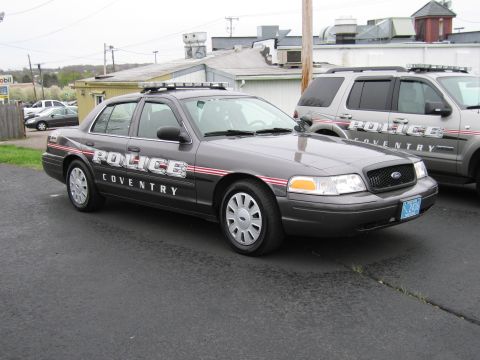 1991 Ford LTD Crown Victoria - gray Ford Crown Victoria marked Coventry Police with red stripes sits in a paved lot beside a matching SUV.